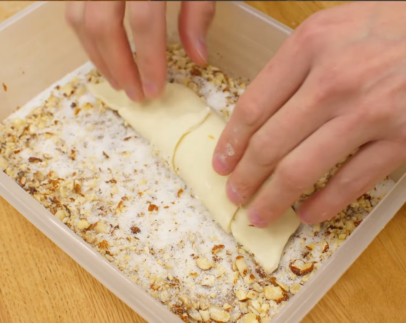 Schritt 15 Die geformten Nussgipfel mit einem Wassersprüher bespritzen und einzeln in der Nuss-Zuckermischung wenden. Danach die Nussgipfel mit genügend Abstand auf ein mit Backpapier belegtes Blech legen. Die Teiglinge mit einem Plastik zudecken und für etwa 30 Min. bei Raumtemperatur abstehen lassen.