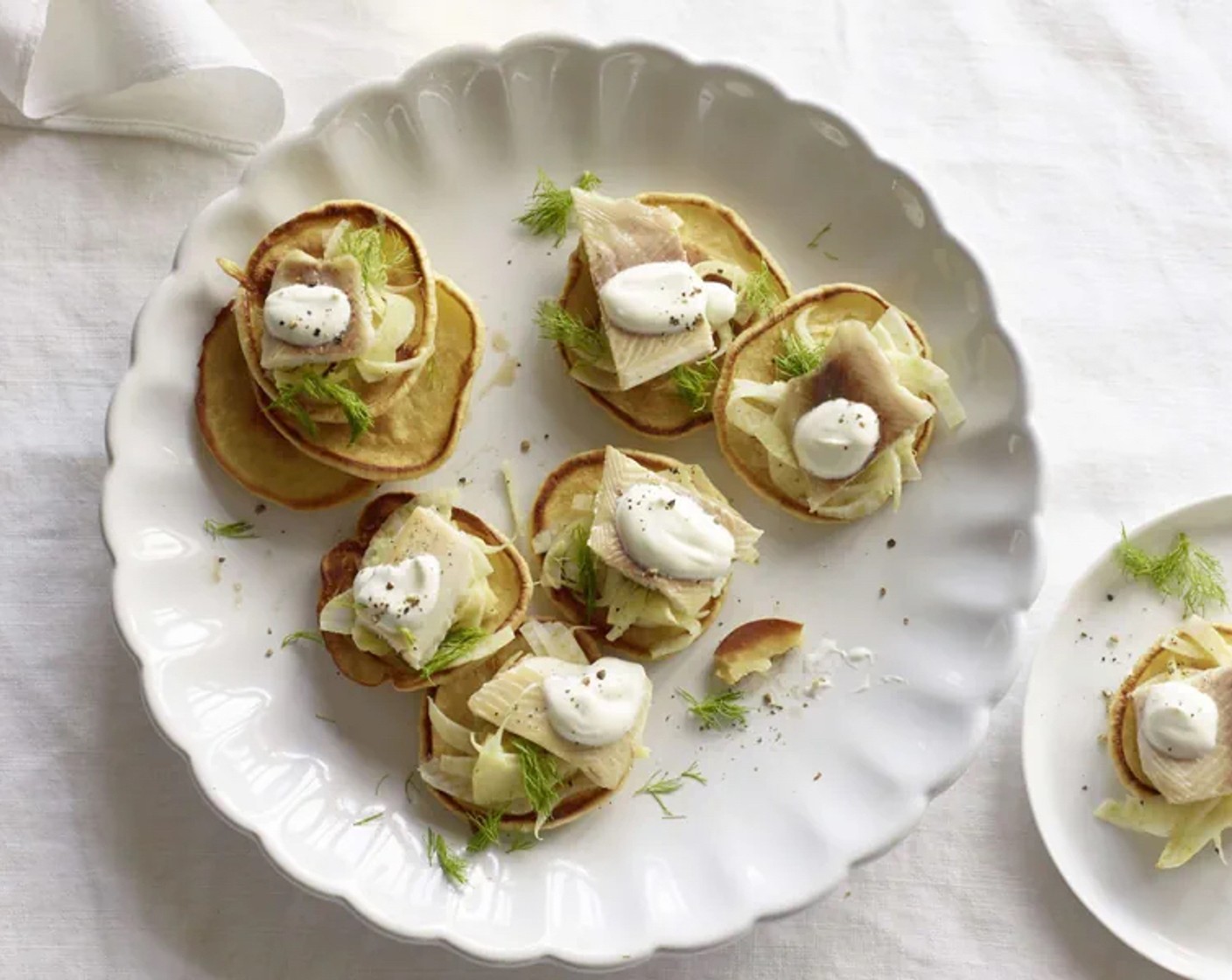 Schritt 4 Den Fenchel auf die Blini verteilen. Rauchforellen (300 g) in Stücke schneiden und daraufgeben. Mit Fenchelgrün und Halbrahm (180 g) servieren.