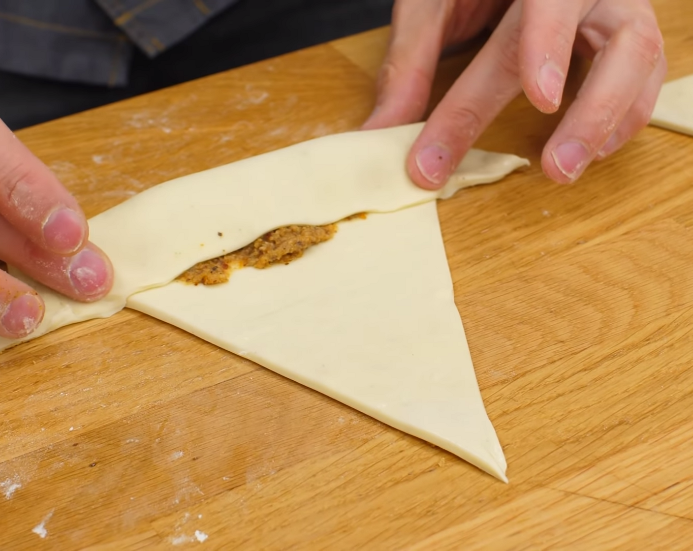 Schritt 13 Mit etwas Wasser alle Verbindungsstücke der Dreiecke leicht bestreichen. Danach die Dreiecke mit der breiten Seite einmal über die Füllung schlagen, dann das Teigstück ganz aufrollen. Dabei das Teigende (den Teigspitz) leicht ziehen, so dass dieser Verschluss dann auf der Unterseite des Nussgipfels ist.