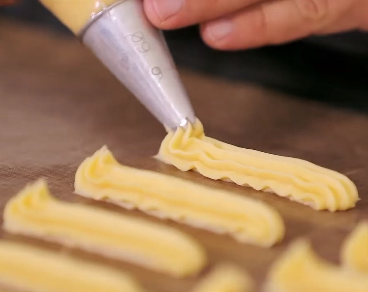 Schritt 3 Ca. 20 Stangen mit 8 cm Länge auf zwei mit Backpapier belegte Kuchenbleche spritzen. Kuchenbleche nacheinander in den vorgeheizten Ofen schieben.