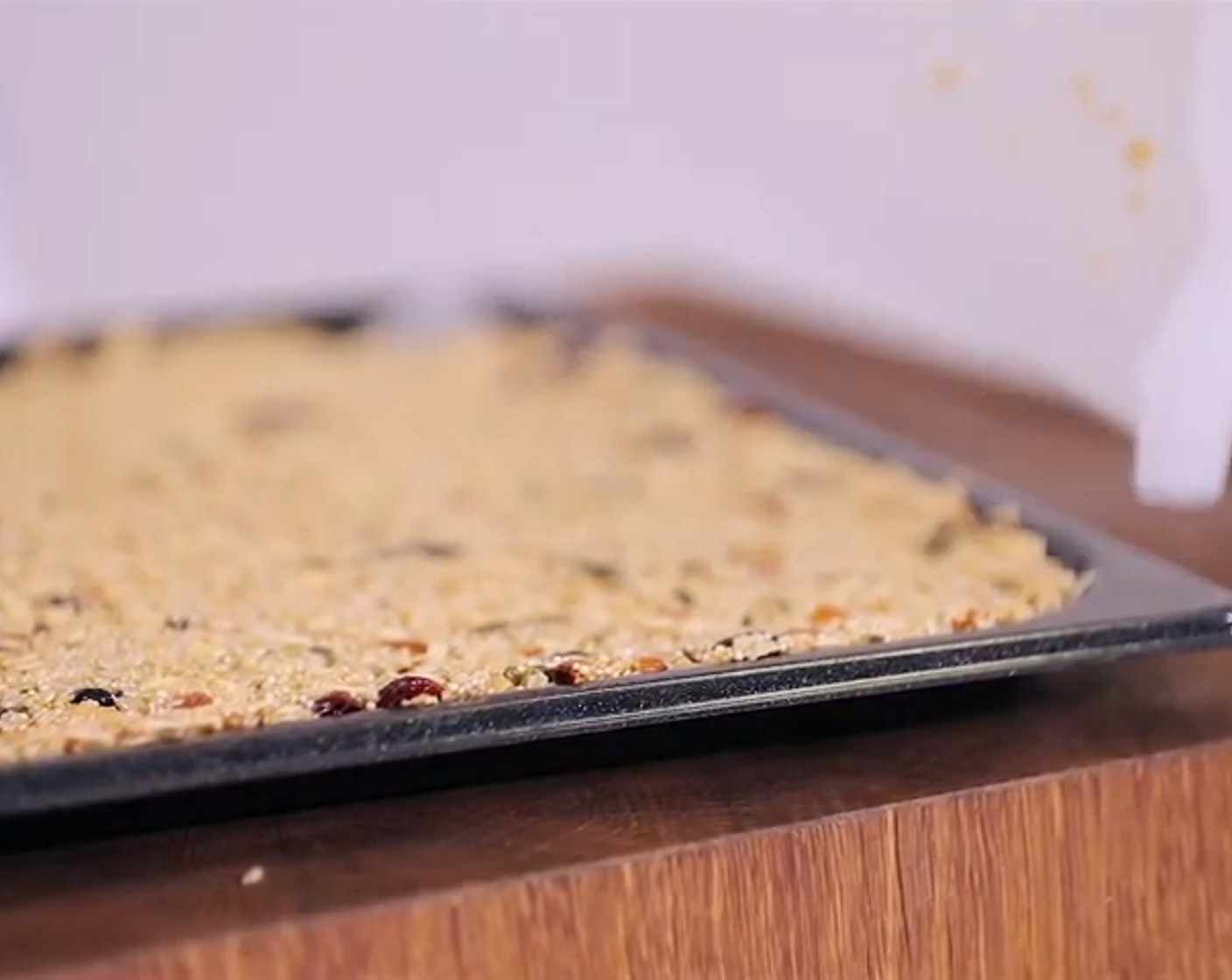 Schritt 8 Als nächstes die Getreidemischung 1,5 cm dick auf ein rechteckiges, mit Backpapier belegtes Kuchenblech verteilen und mit einem zweiten Blech fest andrücken, sodass die Masse richtig kompakt ist. Das Blech auf den Gitterrost in den vorgeheizten Ofen zum Backen schieben.