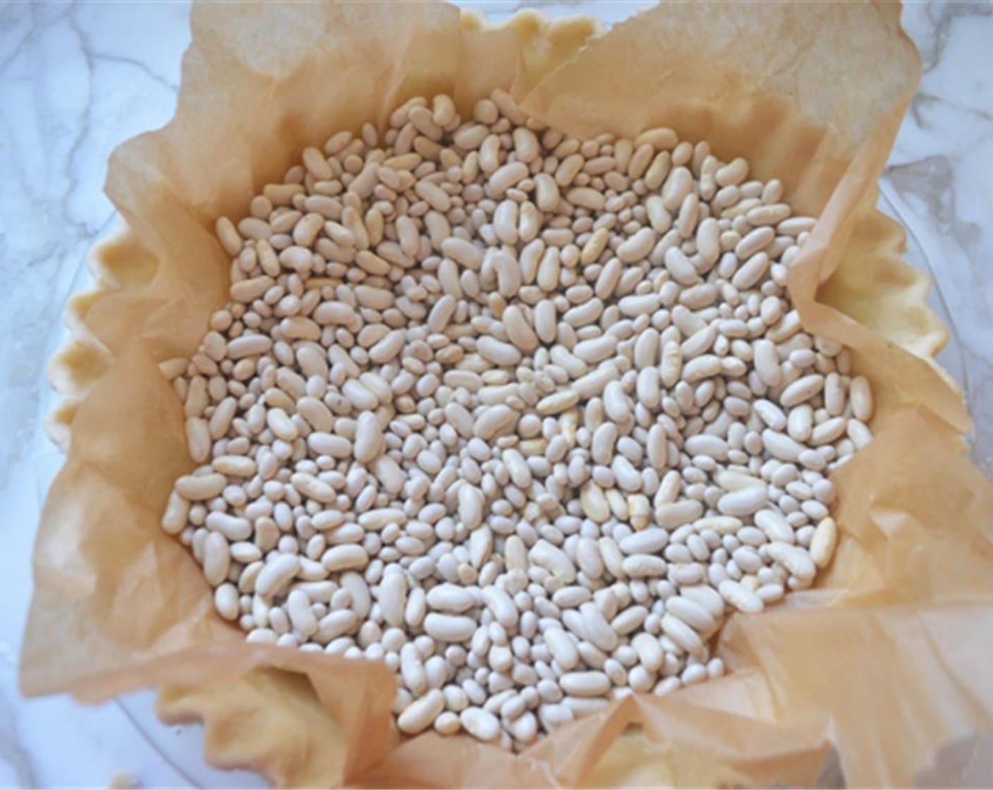 Schritt 9 Den Tortenboden aus dem Gefrierschrank nehmen und ihn auf ein Backblech legen. Den Boden mit einem Stück Backpapier abdecken und zur Hälfte mit getrockneten Bohnen oder Tortengewichten füllen. Den Teig für 25 Minuten blind backen.