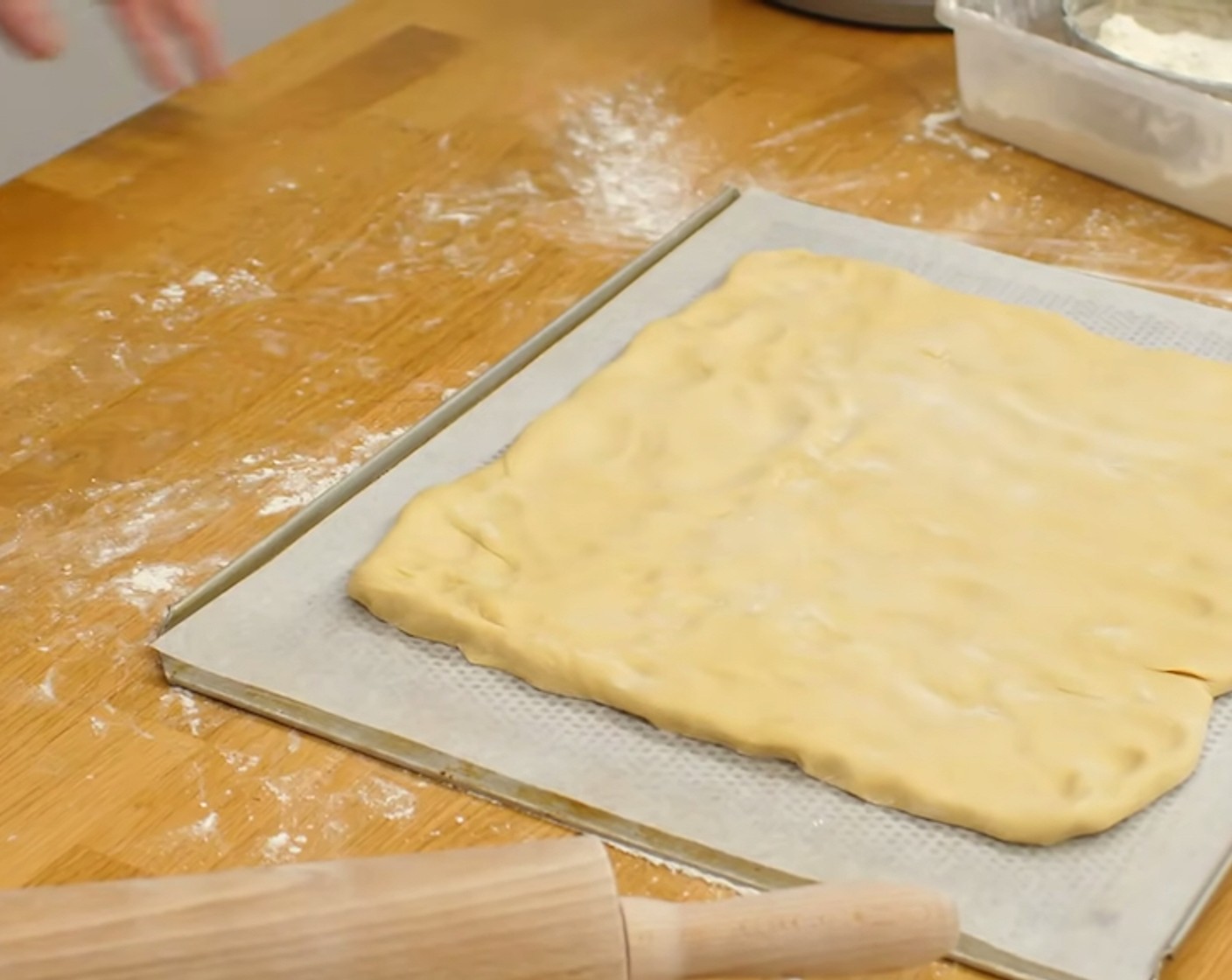 Schritt 14 Den Teig aus dem Becken und auf eine bemehlte Arbeitsfläche stürzen. Dann gleichmässig in eine rechteckige Form drücken und etwa auf 1 cm Dicke ausrollen und auf ein mit Backpapier belegtes Blech legen.