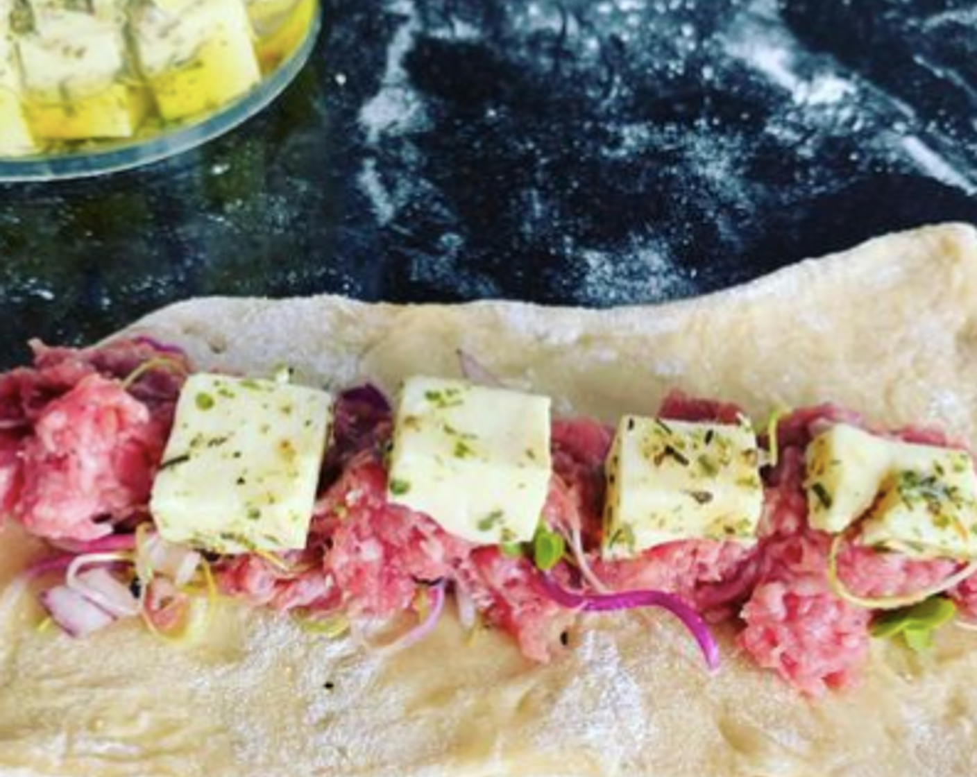 Schritt 5 Als nächstes die Hack-Füllung quer auf einem Teigstück platzieren. Dann Sprossen-Mix (1 Handvoll) und 4 Käse-Würfel (32 Würfel) auf die Masse geben.