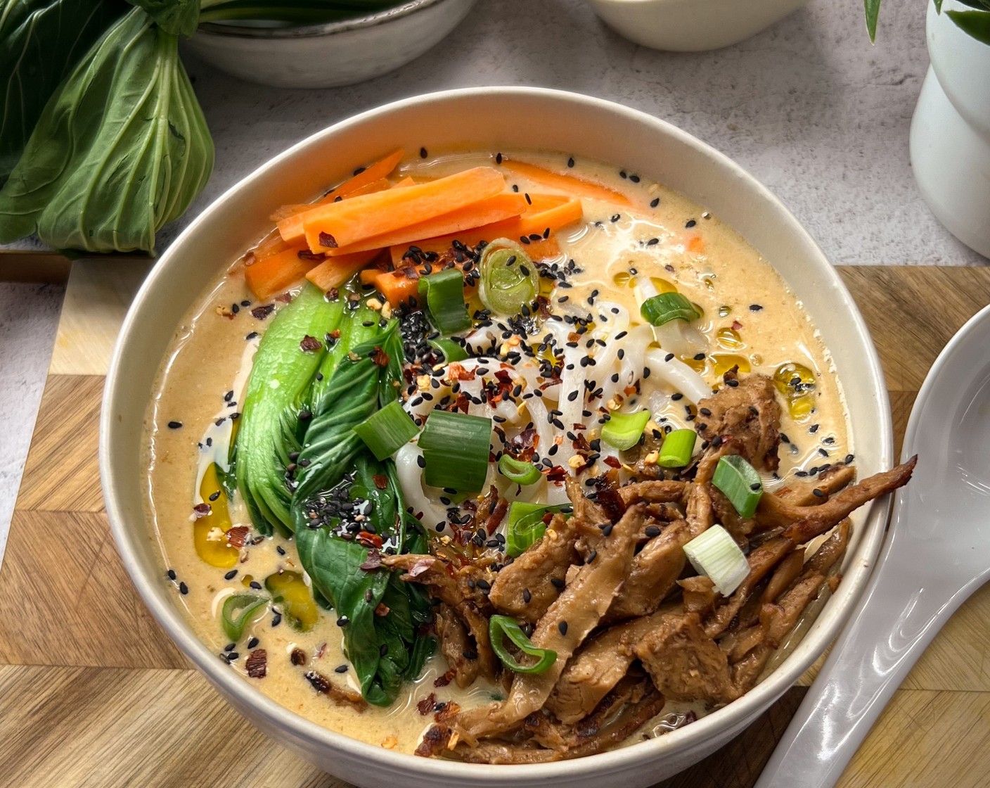 Schritt 5 Servieren: Die Brühe in eine Schüssel geben, die Udon-Nudeln hinzufügen und mit der planted.duck, dem Gemüse (wir haben Pak Choi (wenig) und Karotten (wenig) verwendet) sowie dem grünen Teil der Frühlingszwiebel, etwas Sesamsamen (wenig) und Chiliflocken (wenig) garnieren.