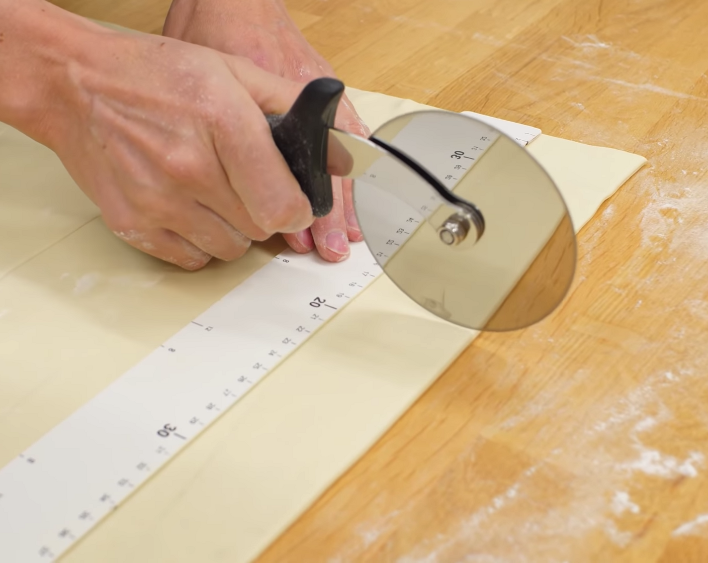 Schritt 10 Danach mit einem Pizzaschneider eine Längsseite gerade abschneiden. Dann aus dem Teig Streifen von 20 cm Länge schneiden; am unteren Rand eine Breite von 18 cm markieren und am oberen Rand die Mitte dieser 18 cm markieren.