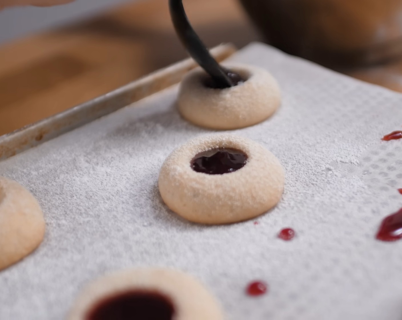 Schritt 8 Die Himbeerkonfitüre (wenig) in einem Kochtopf auf dem Herd erwärmen und dann in einen Spritzbeutel oder einen Dossiertrichter geben. Anschliessend die Mulden der Kekse mit der heissen Marmelade befüllen.
