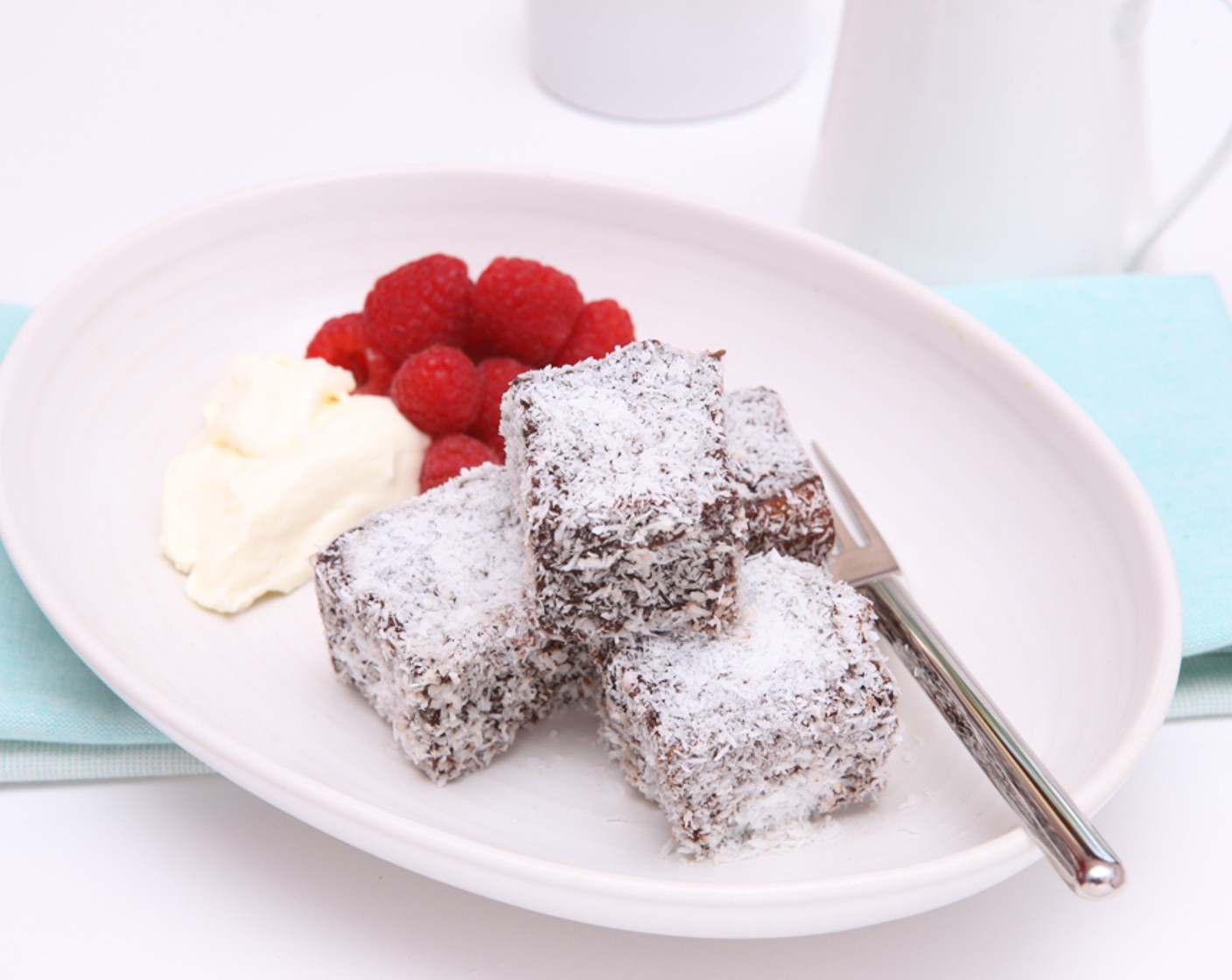 Schritt 9 Garnitur: Zum Schluss den Rahm (300 ml) steif schlagen und zusammen mit den Himbeeren (250 g) mit den Lamingtons servieren.
