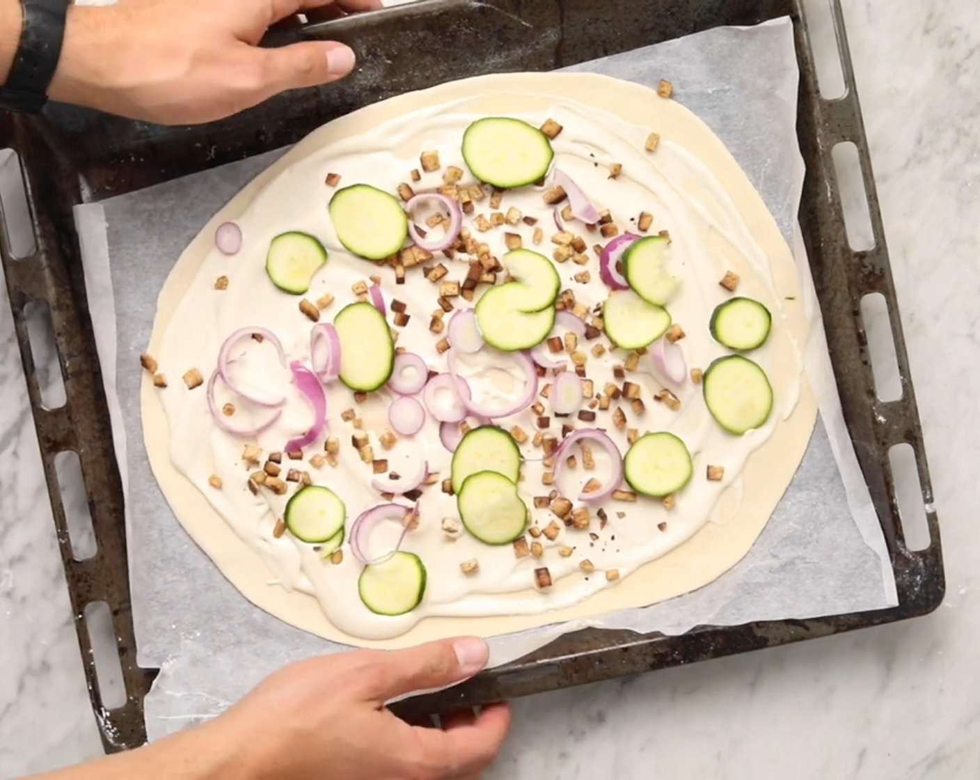 Schritt 7 Den Aufstrich auf dem ausgewallten Teig verteilen. Die Tofuwürfel darüberstreuen. Die Zwiebel (1) in Ringe und die Zucchini (1/4) in Scheiben schneiden und ebenfalls darauf verteilen.