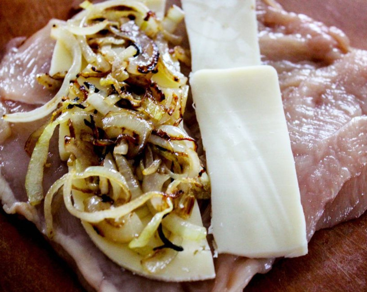 Schritt 6 Sobald das Fleisch plattgedrückt ist, die Frischhaltefolie entfernen und das Poulet mit Schweizer Käse (4 Scheiben), Mozzarella-Käse (4 Scheiben) und Zwiebeln befüllen.
