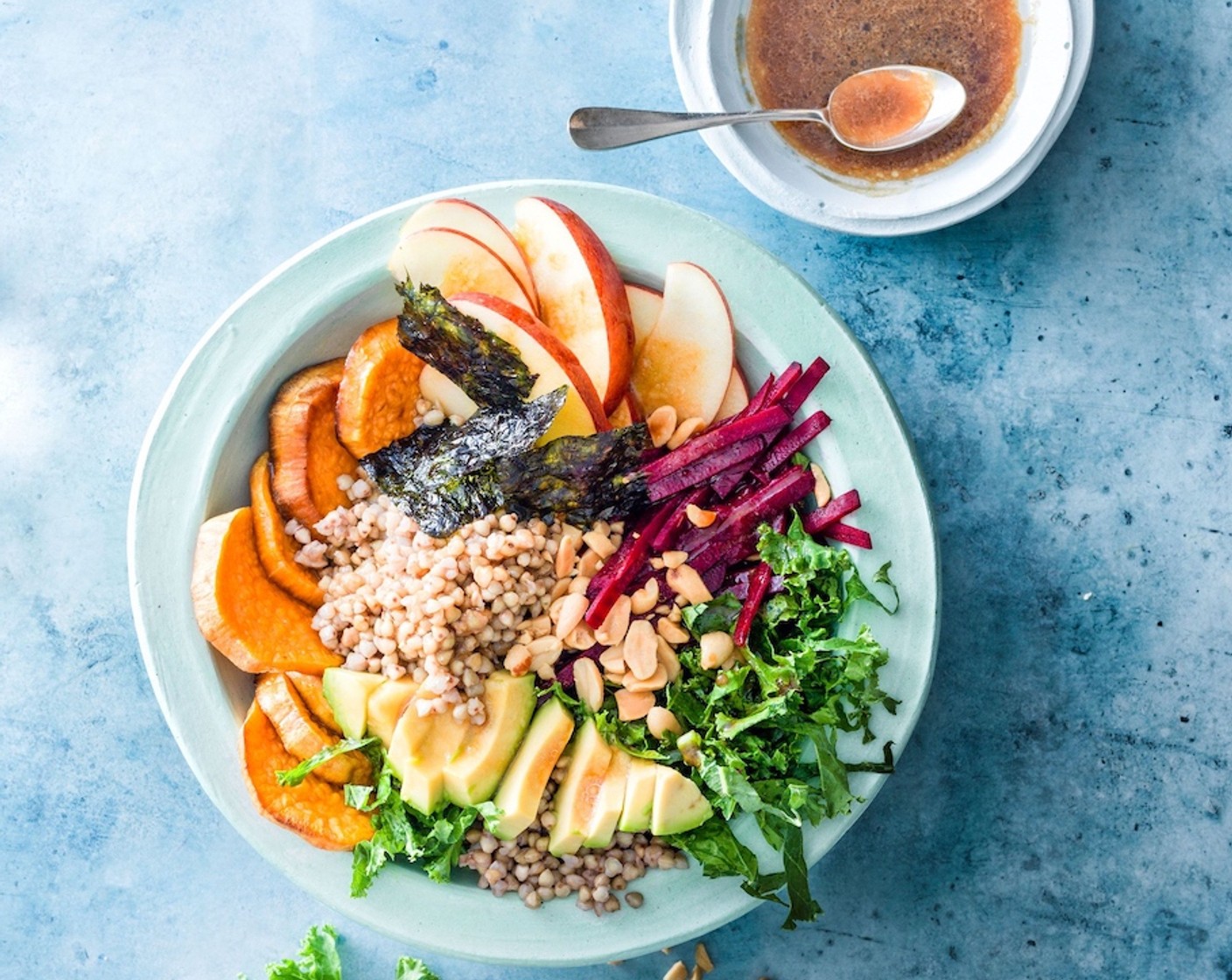 Schritt 6 Den Buchweizen auf die Schüsseln aufteilen und mit Apfelschnitzen, Randen, Federkohl, Avocado und Süsskartoffeln im Uhrzeigersinn belegen. Mit den gerösteten Erdnüssen bestreuen und mit Noriblättern (wenig) ausgarnieren. Zum Schluss die Sauce darüber träufeln und geniessen.