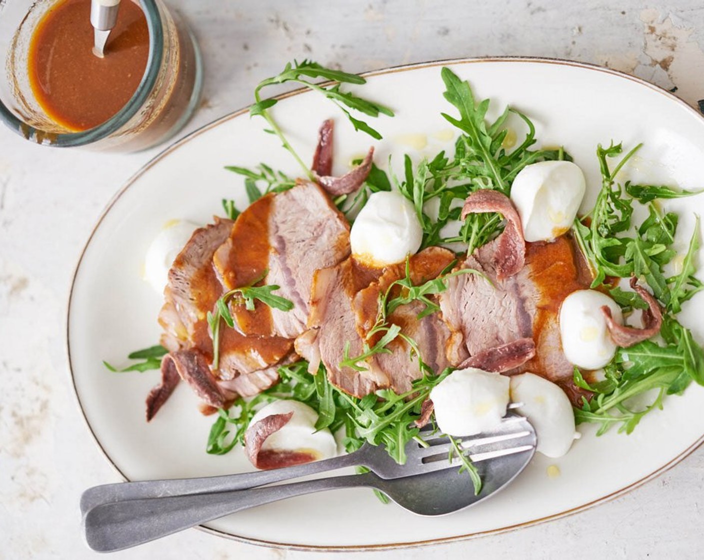 Schritt 6 Das lauwarme Fleisch in dünne Scheiben schneiden und mit Büffelmozzarella, Rucola und Sardellenfilets auf einem Teller oder einer Platte anrichten. Sauce darüber geben und mit Salz und Pfeffer würzen. Zum Schluss mit Olivenöl (2 Esslöffel) beträufeln.