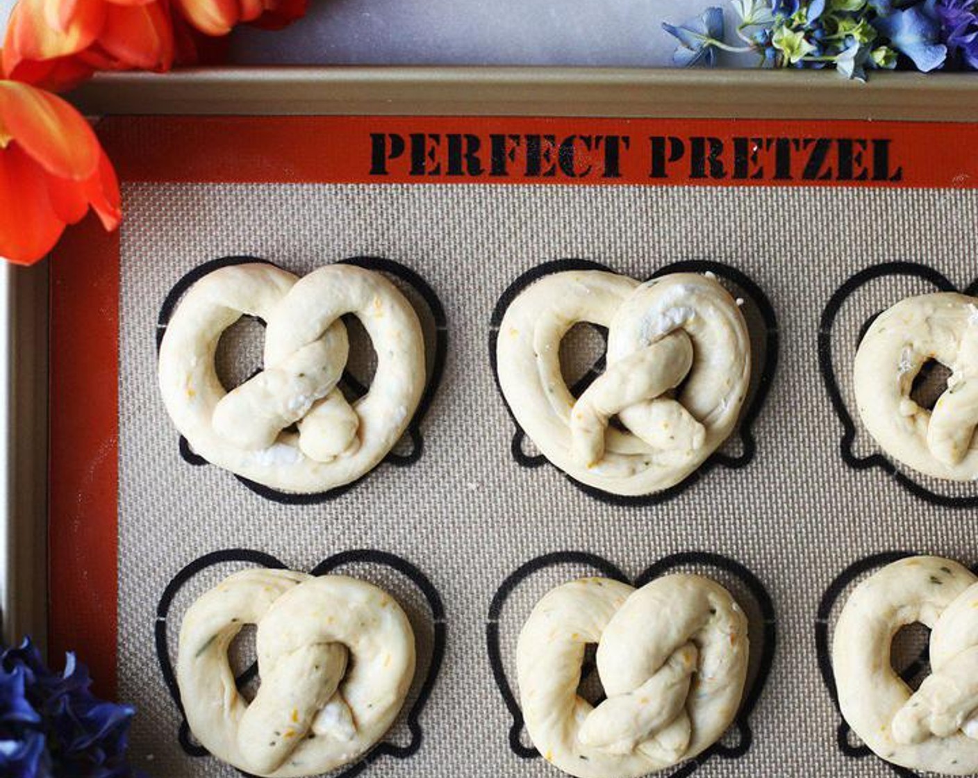 Schritt 8 Jedes Stück zu einem Strang von etwa 30–38 cm Länge ausrollen, wobei die Enden etwas dünner sein sollten. Anschliessend die Brezel formen und auf ein mit Backpapier belegtes Backblech legen. 15 Minuten ruhen lassen.