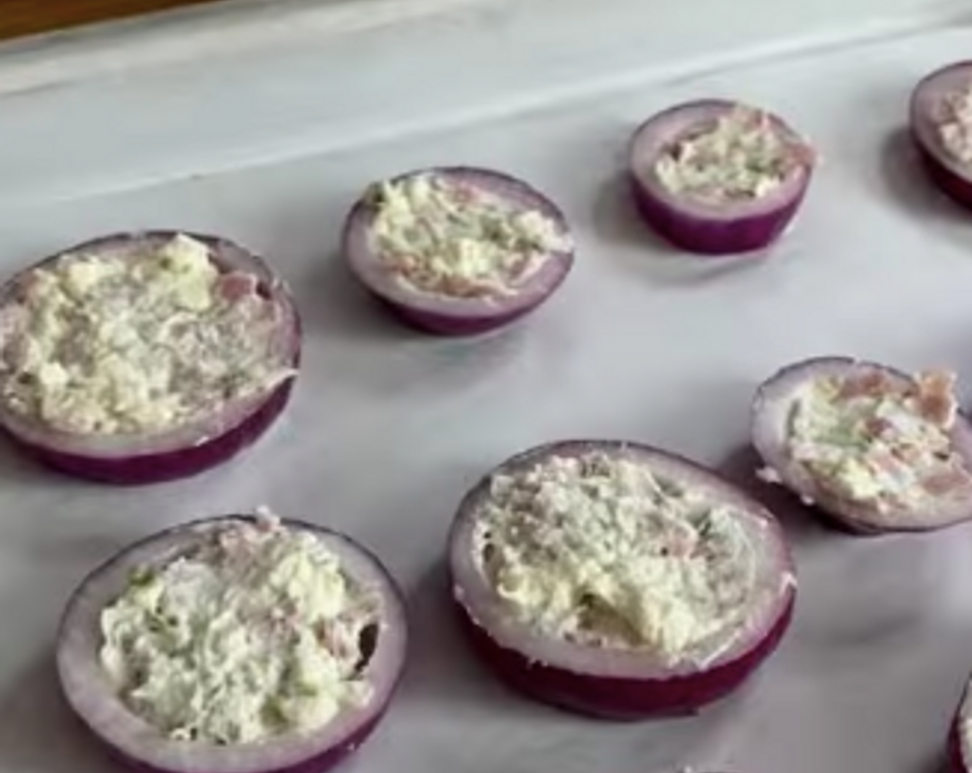 Schritt 3 Die Frischkäse-Masse mit einem Löffel in die Zwiebelringe füllen, auf ein mit Backpapier belegtes Blech legen und für etwa 45 Minuten im Gefrierfach ruhen lassen.