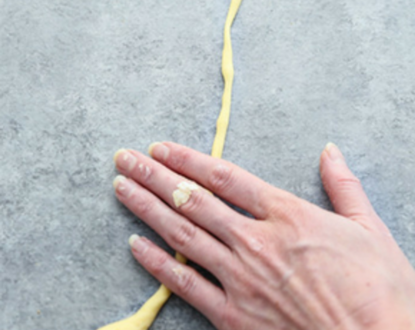 Schritt 4 Den ersten Teig auf die Arbeitsfläche geben und mit feuchten Händen zu einem dicken Zylinder ausrollen. Das Ausrollen der Pici-Pasta erfordert etwas Geschicklichkeit und Gefühl. Den Teig in der linken Hand halten und mit der rechten Hand den rechten Teil der Teigrolle zu einem dünnen Strang rollen. Je dünner, desto besser. Im Idealfall sollte der fertige Strang eine möglichst gleichmässige Grösse haben, damit er gleichmässig gekocht wird.