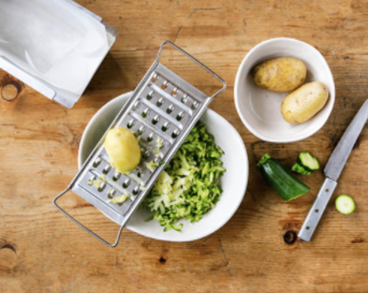 Schritt 2 Eine Kuchenform mit Backpapier auskleiden. Die Zucchini (300 g) an der groben Raffel reiben. In ein sauberes Küchentuch geben und die Flüssigkeit so gut wie möglich herausdrücken. Zucchini in eine grosse Schüssel geben. Die Kartoffeln (300 g) schälen und ebenfalls an der groben Raffel dazureiben.