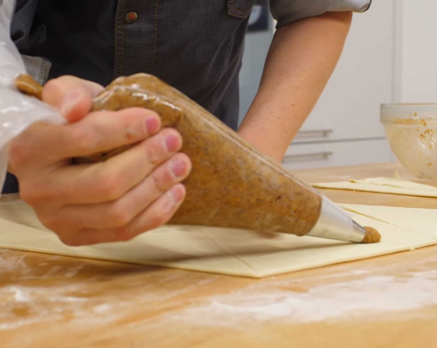 Schritt 12 Anschliessend die Nussfüllung aus dem Kühlschrank nehmen und in einen Spritzbeutel mit einer 12er Lochtülle geben. Danach auf den breiteren Teil des Dreieckes einen Streifen der Nussfüllung spritzen und dabei vom Teigrand her etwa 1 cm Abstand frei lassen.
