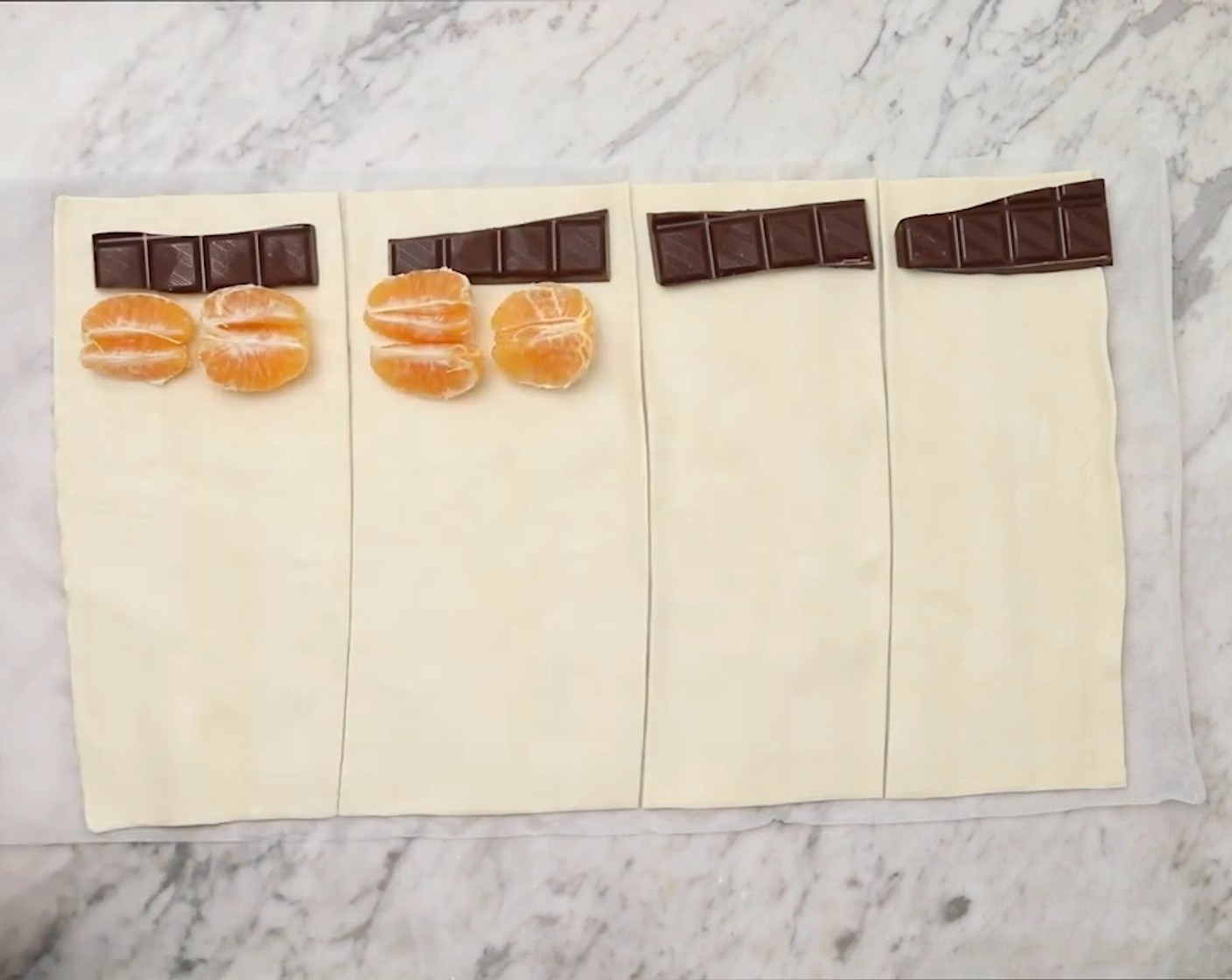 Schritt 3 Am Ende jedes Blätterteigsstreifens ein Stück Schokolade (4 Stück) und zwei Stückchen Mandarinen (2) platzieren. Wer möchte, kann die Schokolade auch halbieren, so dass zwei feine Schokoladenstränge entstehen.