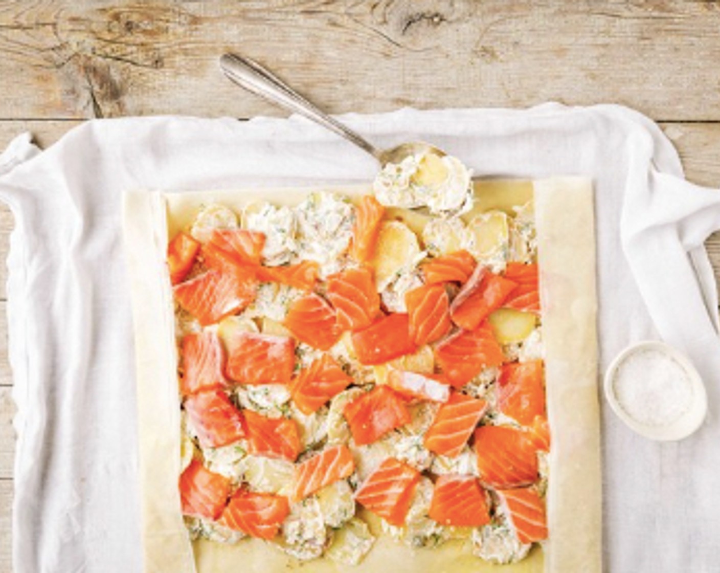 Schritt 4 Die unteren 2/3 des Teiges mit Paniermehl (2 Esslöffel) bestreuen. Die Kartoffelfüllung darüber geben. Die Lachsstücke darauf verteilen, dabei auf beiden Seiten einen Rand von ca. 4 cm frei lassen. Seitliche Ränder einschlagen. Das Tuch leicht anheben, Strudel locker aufrollen, mit dem Verschluss nach unten auf ein mit Backpapier belegtes Blech legen.
