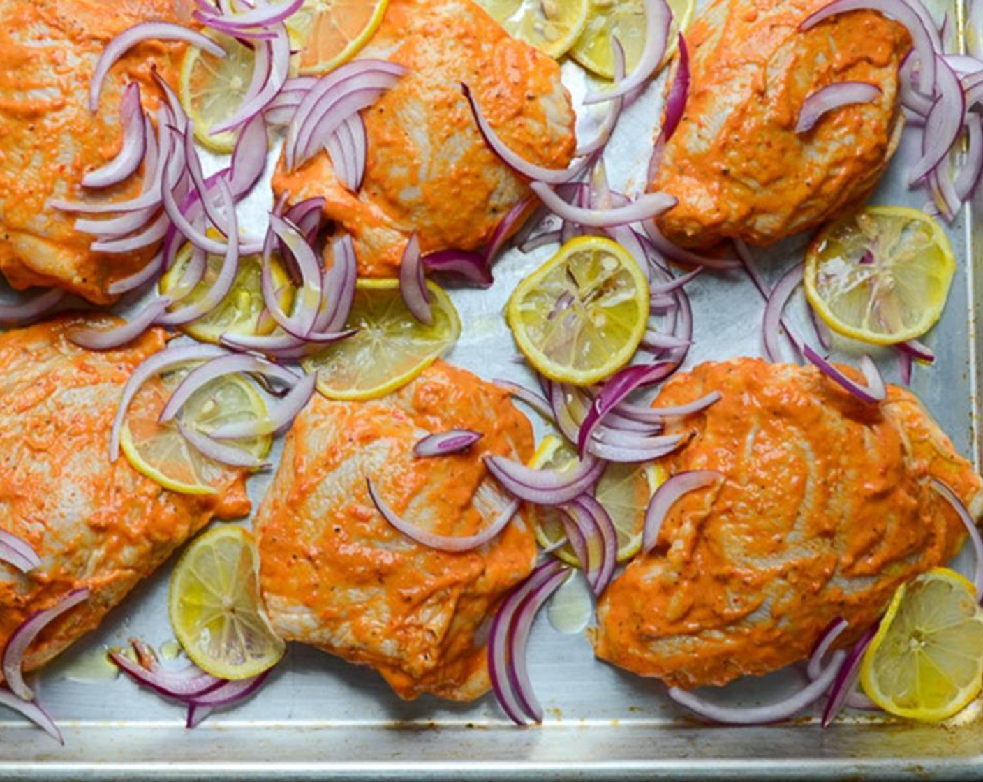 Schritt 10 Backofen auf 220 °C (425 °F) vorheizen. Zwiebel (1) schälen und in dünne Spalten schneiden. Zitrone (1) in 6 dünne Scheiben schneiden. Die Hähnchenschenkel mit ausreichend Abstand auf ein grosses Backblech legen. Die Zwiebelstücke über das Hähnchen verteilen. Auf jeden Schenkel eine Zitronenscheibe legen.