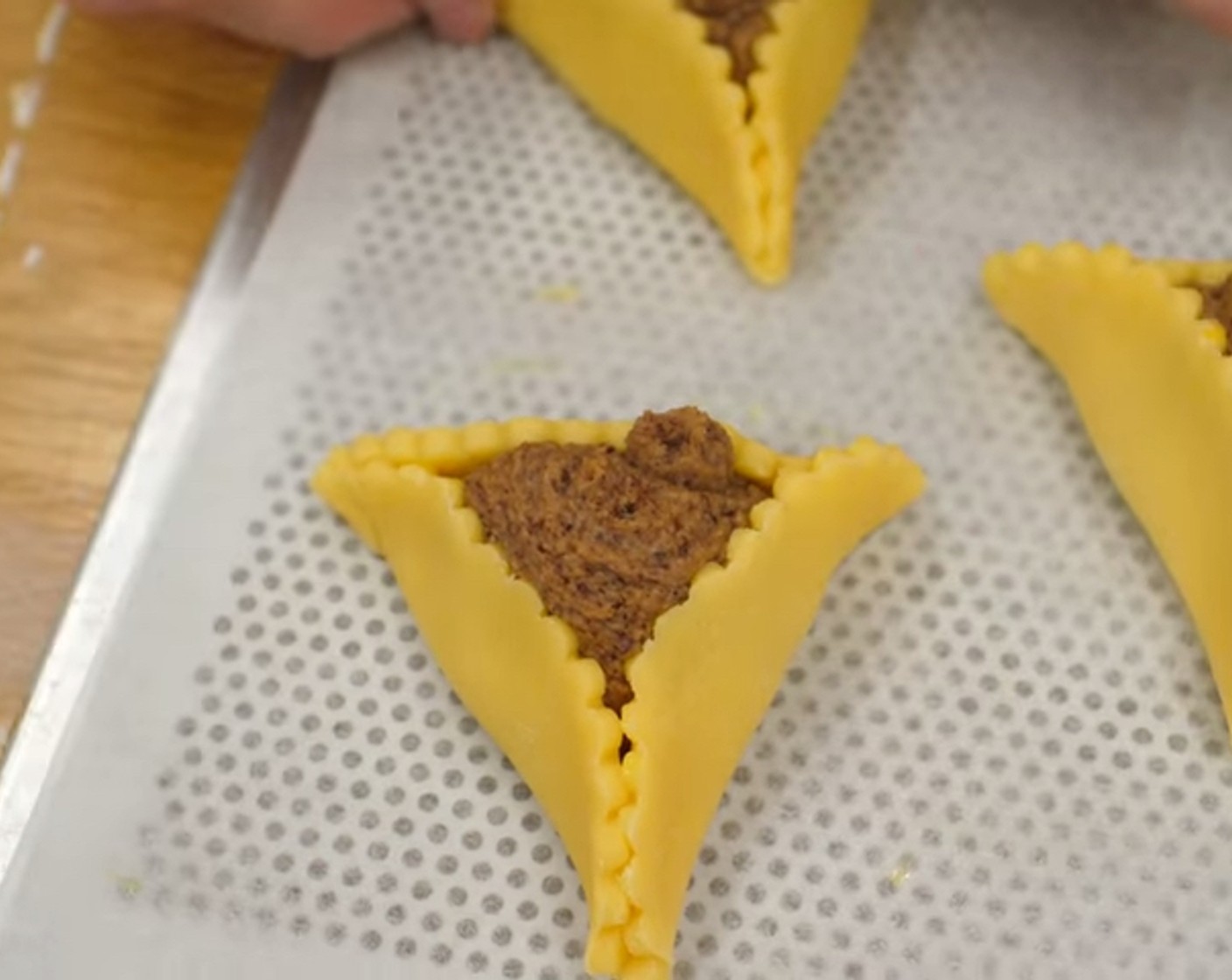 Schritt 11 Anschliessend jeweils drei Seiten der Pfaffenhüte nach oben über die Füllung klappen, so dass eine Dreiecksform entsteht. Dabei muss die Nussfüllung noch zu sehen sein. Die Teigenden, bzw. die Teigspitzen etwas zusammen kneifen.